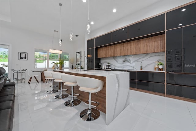 kitchen featuring modern cabinets, hanging light fixtures, a kitchen island with sink, a kitchen bar, and a sink