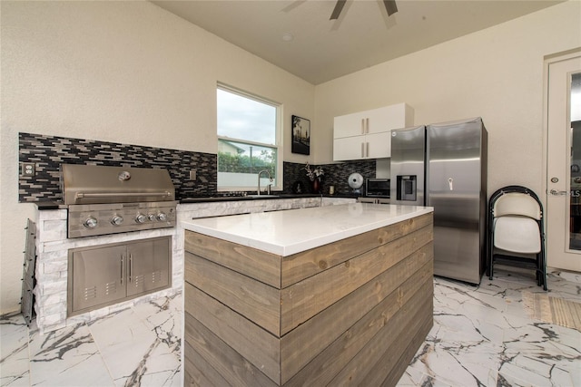 kitchen with marble finish floor, tasteful backsplash, light countertops, a kitchen island, and stainless steel fridge with ice dispenser