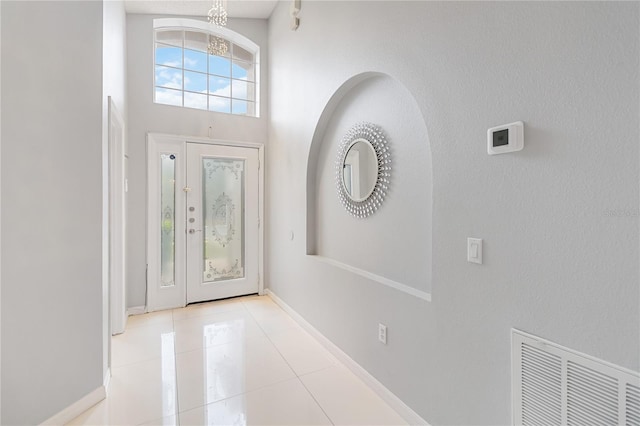 tiled foyer entrance featuring a towering ceiling, baseboards, visible vents, and a notable chandelier