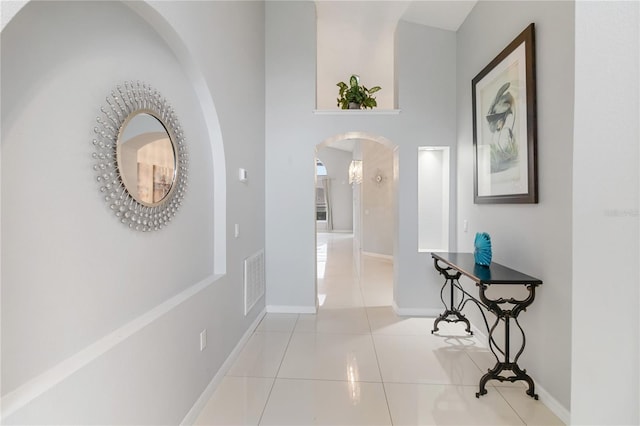 hallway featuring arched walkways, tile patterned flooring, visible vents, and baseboards