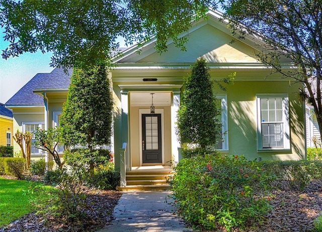 property entrance with stucco siding and a shingled roof