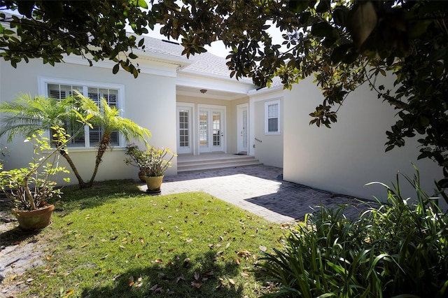 rear view of house featuring french doors, a lawn, and stucco siding