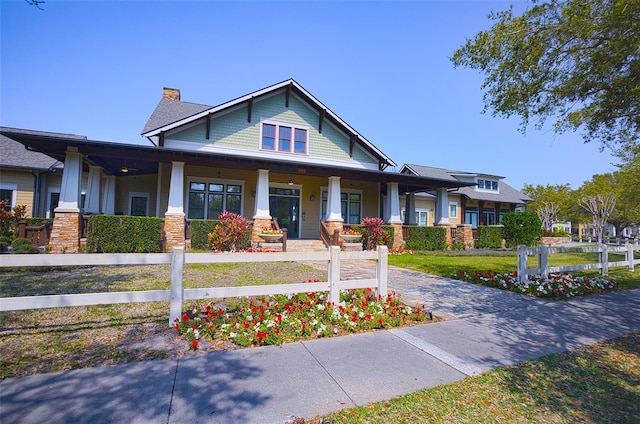 view of front of home featuring a front lawn, stone siding, a porch, fence, and a chimney