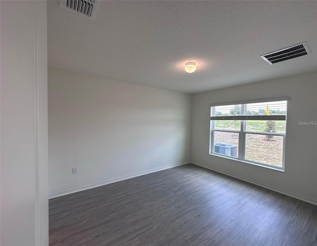 spare room featuring a textured ceiling, dark wood-type flooring, visible vents, and baseboards