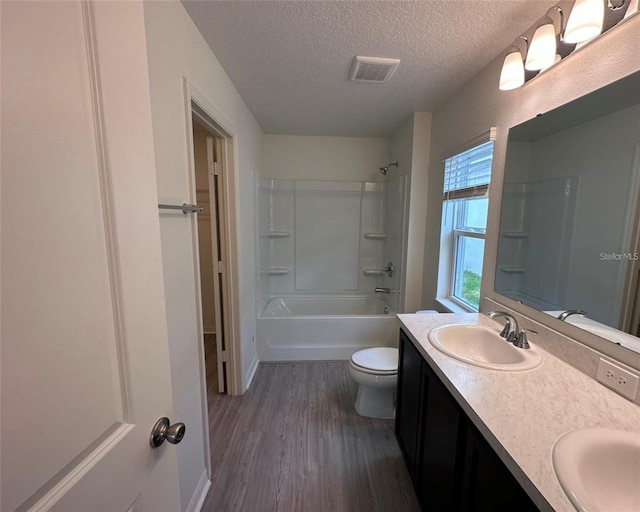 bathroom with double vanity, visible vents, a sink, a textured ceiling, and wood finished floors