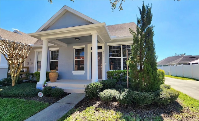 view of front of house featuring covered porch, a shingled roof, fence, and stucco siding