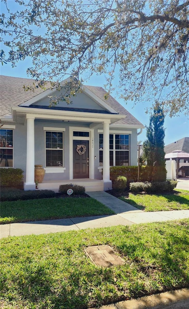 view of front of home with a porch, roof with shingles, a front yard, and stucco siding