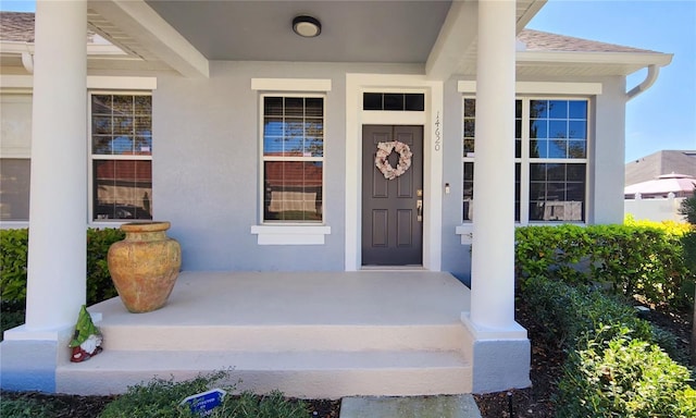 property entrance featuring a shingled roof and stucco siding