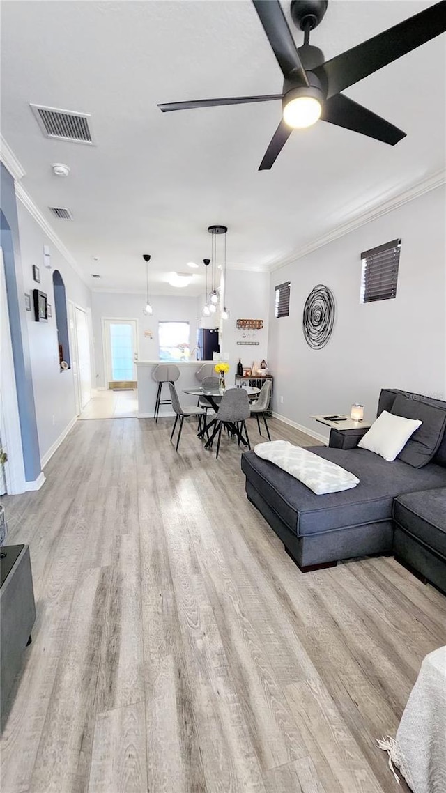 living area with light wood-style flooring, visible vents, arched walkways, and crown molding