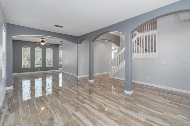 unfurnished living room featuring arched walkways, stairs, visible vents, and baseboards