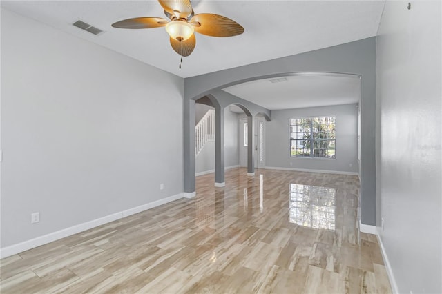 unfurnished living room featuring arched walkways, visible vents, baseboards, and wood finished floors