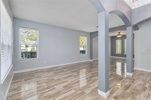 unfurnished living room with a ceiling fan, arched walkways, a textured ceiling, and baseboards