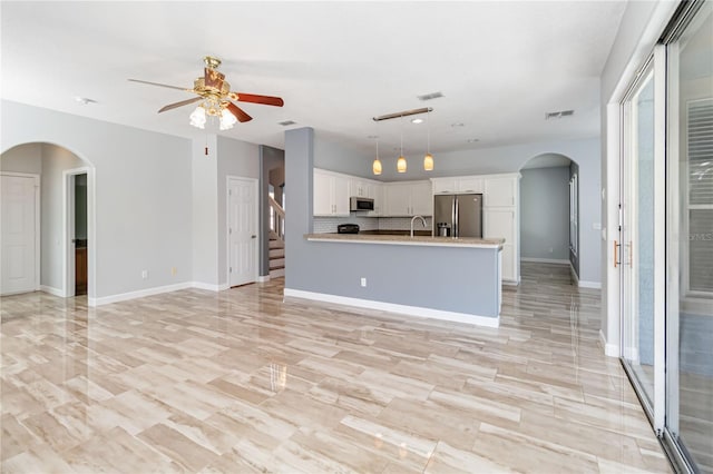 unfurnished living room featuring visible vents, stairs, arched walkways, and baseboards