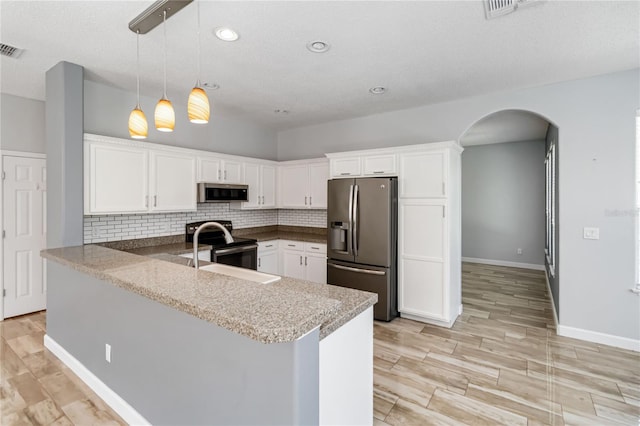 kitchen with arched walkways, a peninsula, a sink, stainless steel appliances, and backsplash