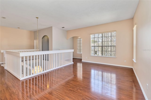 spare room with arched walkways, wood finished floors, and baseboards