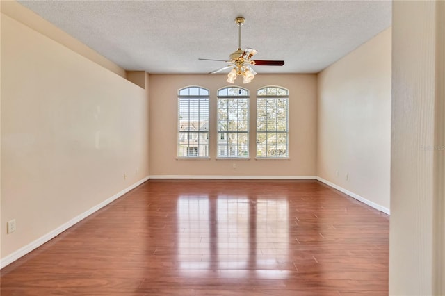 unfurnished room with ceiling fan, a textured ceiling, baseboards, and wood finished floors