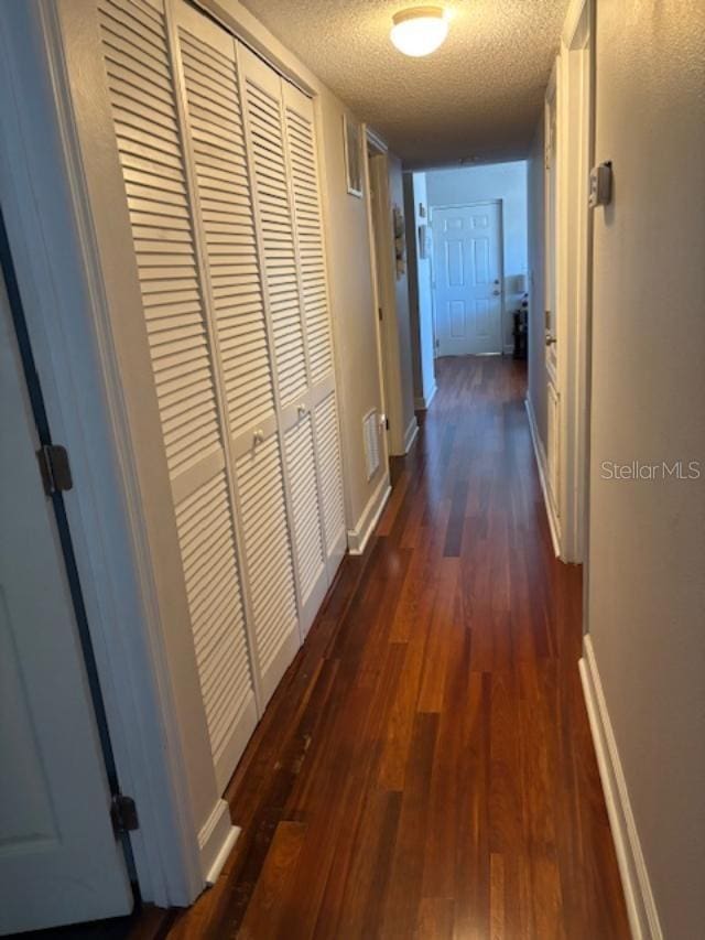 hall featuring a textured ceiling, dark wood finished floors, visible vents, and baseboards