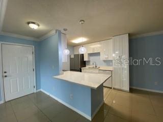 kitchen with white cabinets, ornamental molding, freestanding refrigerator, a peninsula, and light countertops