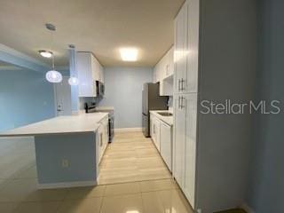 kitchen featuring light tile patterned flooring, a peninsula, white cabinets, light countertops, and appliances with stainless steel finishes