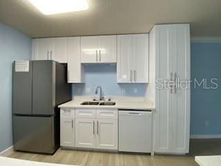 kitchen featuring white dishwasher, light countertops, a sink, and freestanding refrigerator