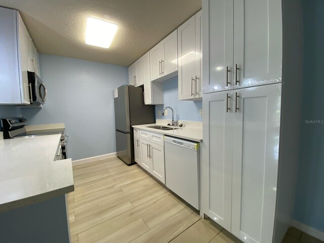 kitchen with white cabinets, stainless steel appliances, a textured ceiling, light wood-style floors, and a sink