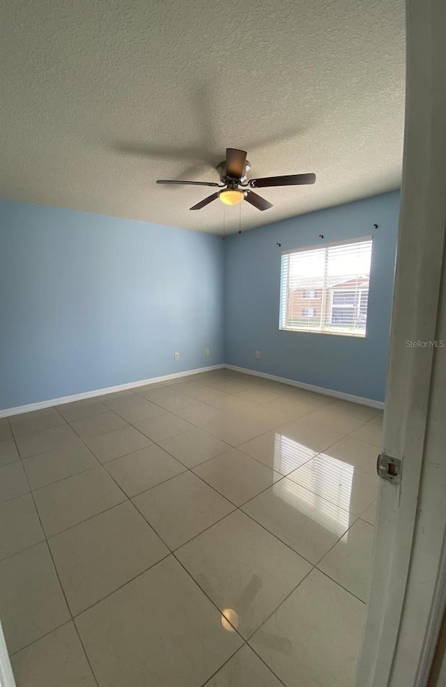 empty room featuring ceiling fan, a textured ceiling, light tile patterned flooring, and baseboards