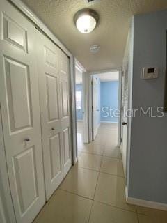 corridor featuring baseboards, a textured ceiling, and light tile patterned flooring