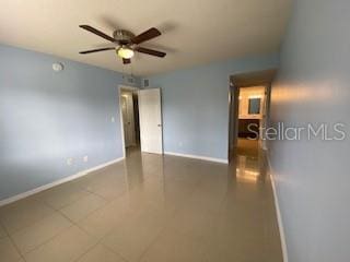 tiled empty room with baseboards and a ceiling fan