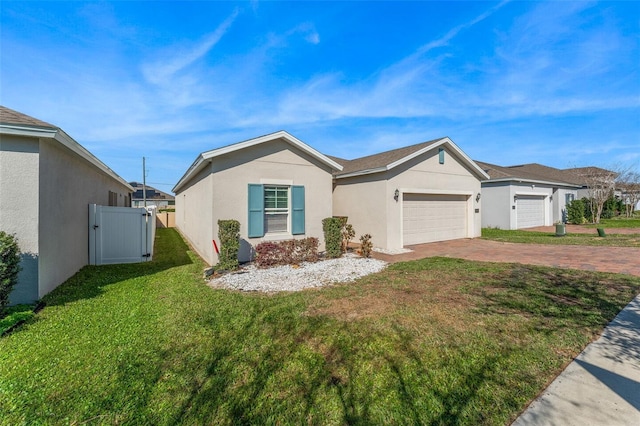 ranch-style house featuring an attached garage, a gate, decorative driveway, a front lawn, and stucco siding