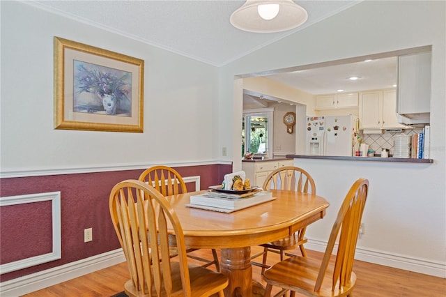 dining area with light wood-type flooring, lofted ceiling, ornamental molding, and baseboards