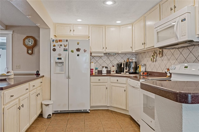 kitchen featuring light tile patterned floors, white appliances, cream cabinetry, decorative backsplash, and dark countertops