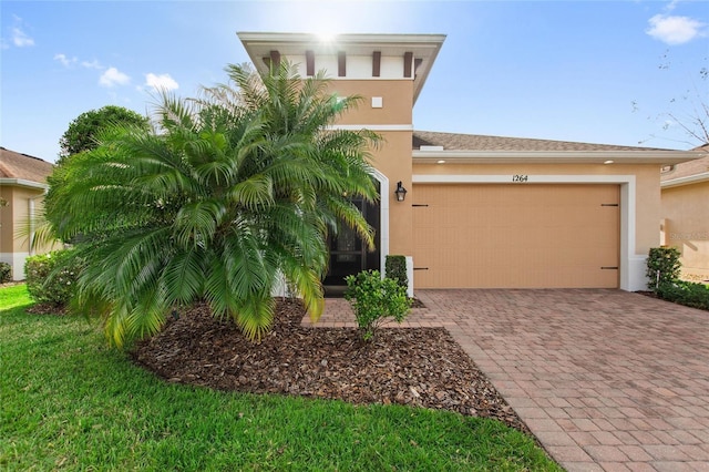 view of front of house featuring decorative driveway, an attached garage, a front yard, and stucco siding