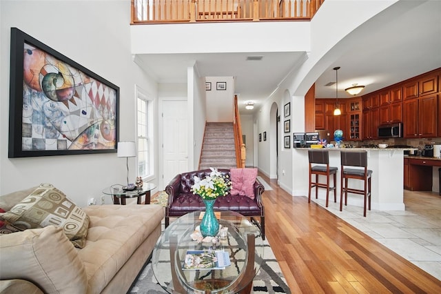 living area with light wood-style flooring, a high ceiling, visible vents, baseboards, and stairway