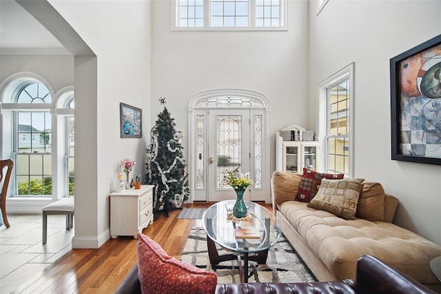 living room with crown molding, a high ceiling, baseboards, and light wood-style floors