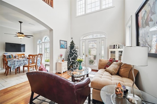 living area with arched walkways, crown molding, a high ceiling, ceiling fan, and light wood-type flooring