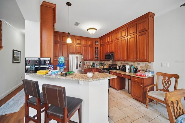 kitchen with appliances with stainless steel finishes, glass insert cabinets, light stone counters, hanging light fixtures, and a peninsula