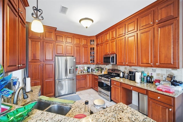 kitchen featuring a sink, appliances with stainless steel finishes, backsplash, light stone countertops, and pendant lighting