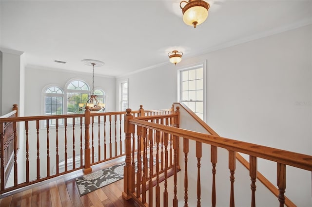 hallway with crown molding, a notable chandelier, visible vents, an upstairs landing, and wood finished floors