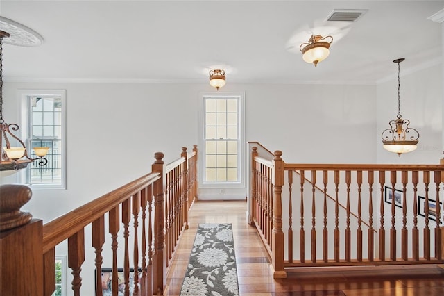 hall with visible vents, wood finished floors, crown molding, an upstairs landing, and a wealth of natural light