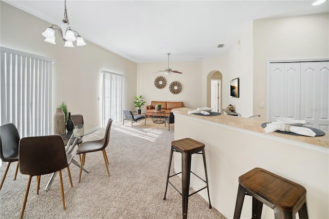 dining space with light carpet, ceiling fan with notable chandelier, arched walkways, and visible vents