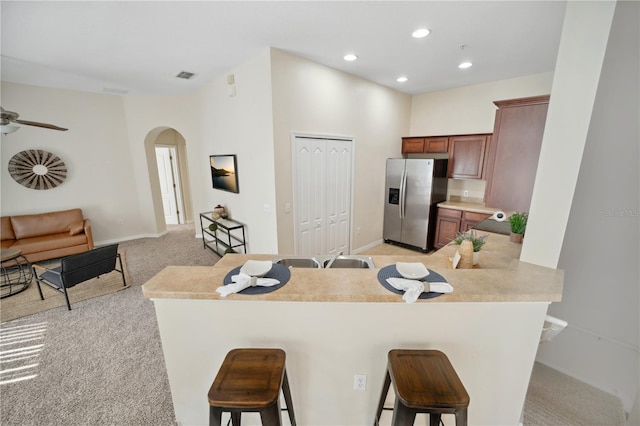 kitchen featuring arched walkways, light colored carpet, light countertops, stainless steel fridge with ice dispenser, and a kitchen bar