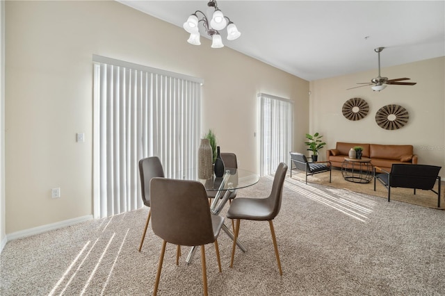 carpeted dining space with ceiling fan with notable chandelier and baseboards