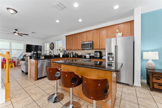 kitchen with light tile patterned floors, visible vents, appliances with stainless steel finishes, dark stone counters, and brown cabinetry