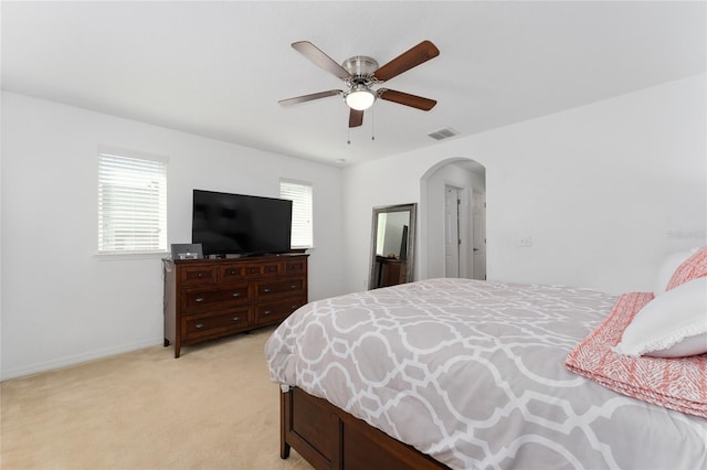 bedroom featuring visible vents, arched walkways, baseboards, light colored carpet, and ceiling fan