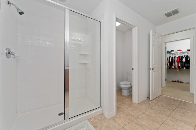 bathroom featuring tile patterned flooring, toilet, visible vents, a spacious closet, and a stall shower