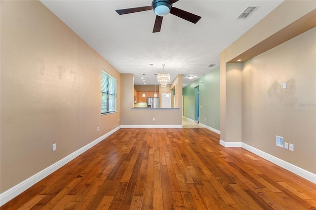 unfurnished living room with visible vents, baseboards, ceiling fan with notable chandelier, and hardwood / wood-style flooring