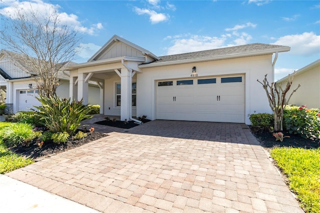 view of front of house featuring an attached garage, board and batten siding, decorative driveway, and stucco siding