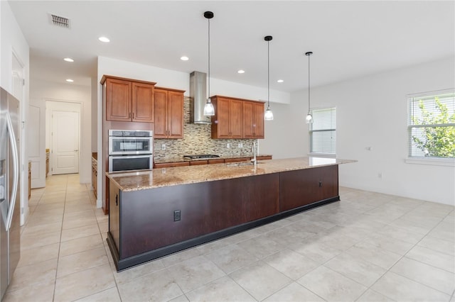 kitchen featuring visible vents, appliances with stainless steel finishes, a sink, wall chimney range hood, and backsplash