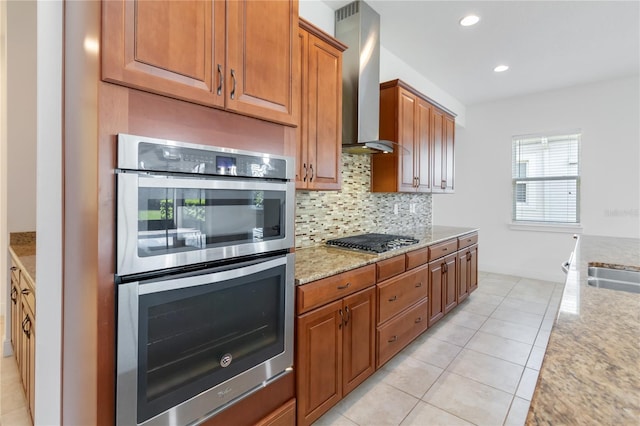 kitchen with light tile patterned floors, stainless steel appliances, decorative backsplash, light stone countertops, and wall chimney exhaust hood