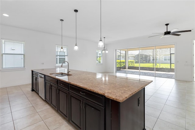 kitchen featuring light tile patterned floors, a kitchen island with sink, a sink, open floor plan, and stainless steel dishwasher